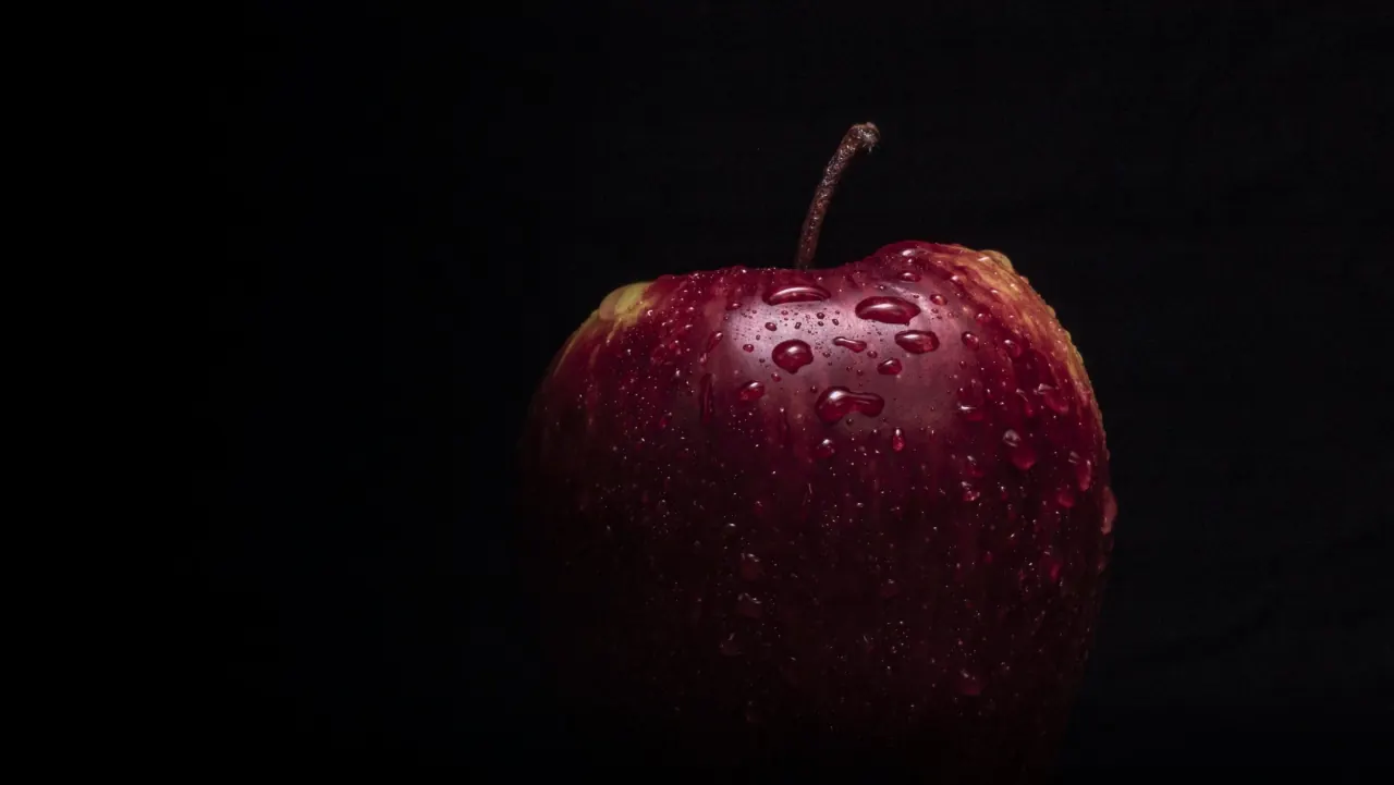 A red apple covered in water droplets, on black